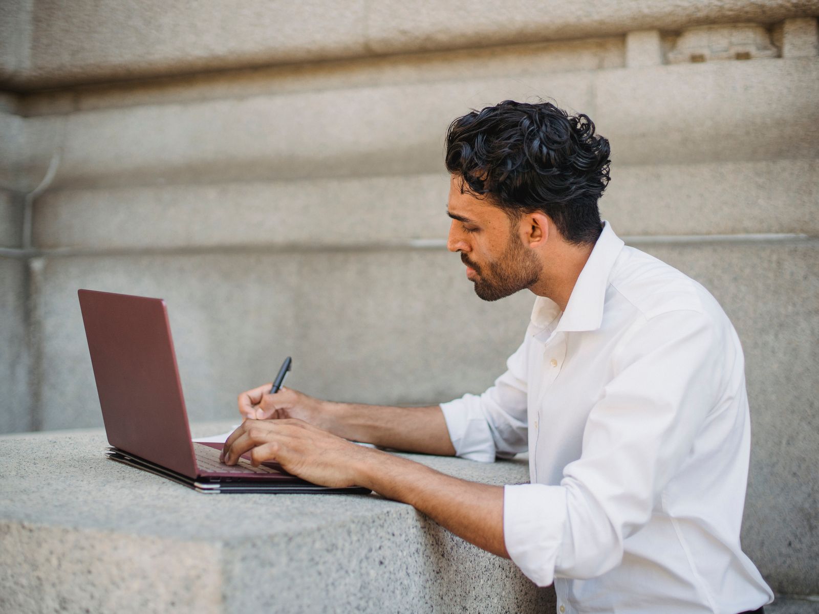 A person taking notes while working at a laptop